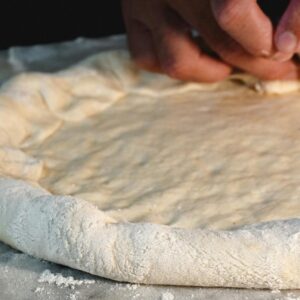 A close-up view of hands preparing pizza dough on a marble surface, showcasing the art of homemade pizza making.