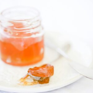 A close-up shot of orange marmalade in a jar, with a spoon on a white plate.